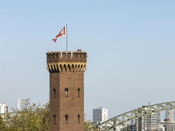 Malakoff Tower The Malakoff Tower in Cologne rises majestically against the backdrop of the river. The striking brick tower with its battlements and flag harmoniously combines historical architecture and a modern view of the Rhine.