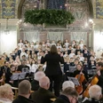 Orchester mit Chor in historischer Kirche, festlich geschmückt für Advent und Weihnacht.