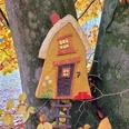 Foto-Flyer-82fa702e-6e4e3d30@800w.jpg Ein buntes, kleines Holzhäuschen hängt an einem Baum, umgeben von leuchtend gelbem Herbstlaub.