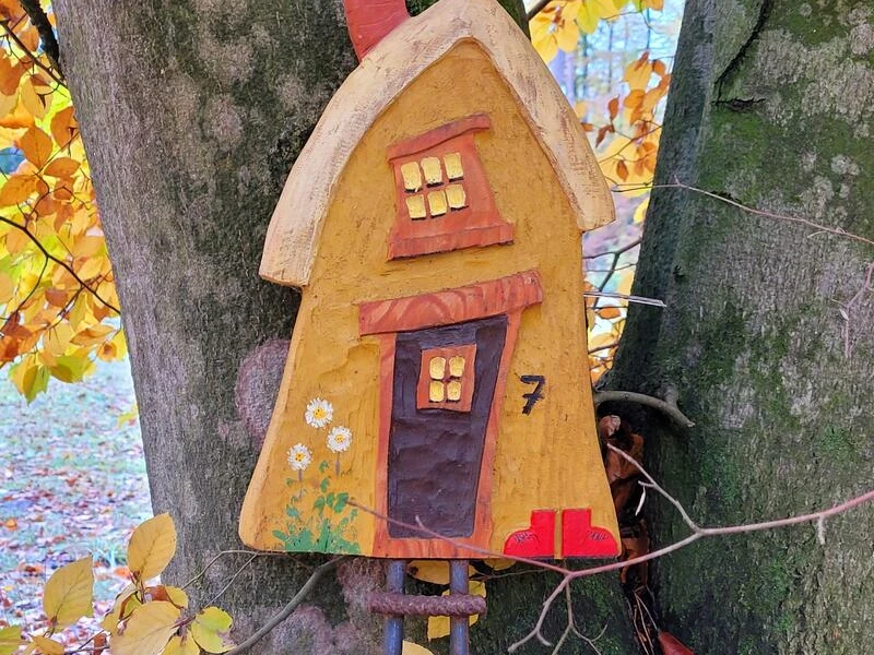 Foto-Flyer-82fa702e-6e4e3d30@800w.jpg Ein buntes, kleines Holzhäuschen hängt an einem Baum, umgeben von leuchtend gelbem Herbstlaub.