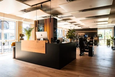 Eingangsbereich Circleone Moderner Empfangsbereich eines Fitnessstudios mit Holz- und Metallelementen, hellem Boden und Pflanzen.