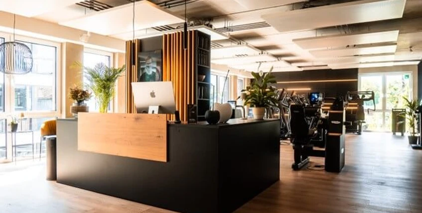 Eingangsbereich Circleone Moderner Empfangsbereich eines Fitnessstudios mit Holz- und Metallelementen, hellem Boden und Pflanzen.