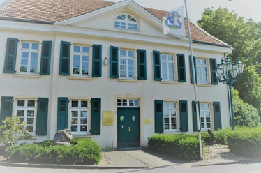 Deusser Haus in Monheim am Rhein Historisches Gebäude mit grün-weißen Fensterläden, blauer Eingangstür und Nordrhein-Westfalen-Flagge.