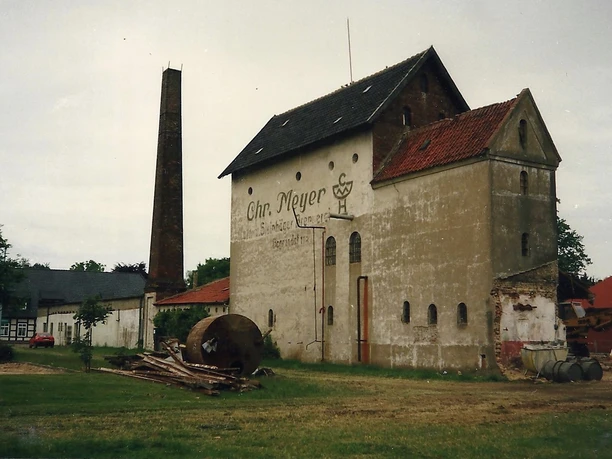Historische Backsteinstruktur mit abgestützten Fassaden und hohem Schornstein, verlassene Umgebung.