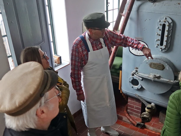 Alte Brennerei szenische Führung mit Erwin.JPG Erwin leitet eine Gruppe durch eine historische Brennerei, zeigt Details eines antiken Kessels.
