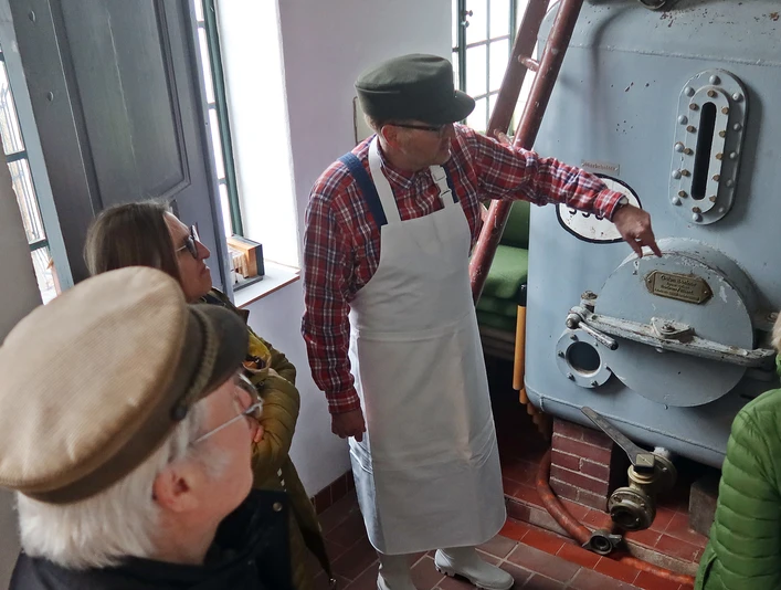 Alte Brennerei szenische Führung mit Erwin.JPG Erwin leitet eine Gruppe durch eine historische Brennerei, zeigt Details eines antiken Kessels.