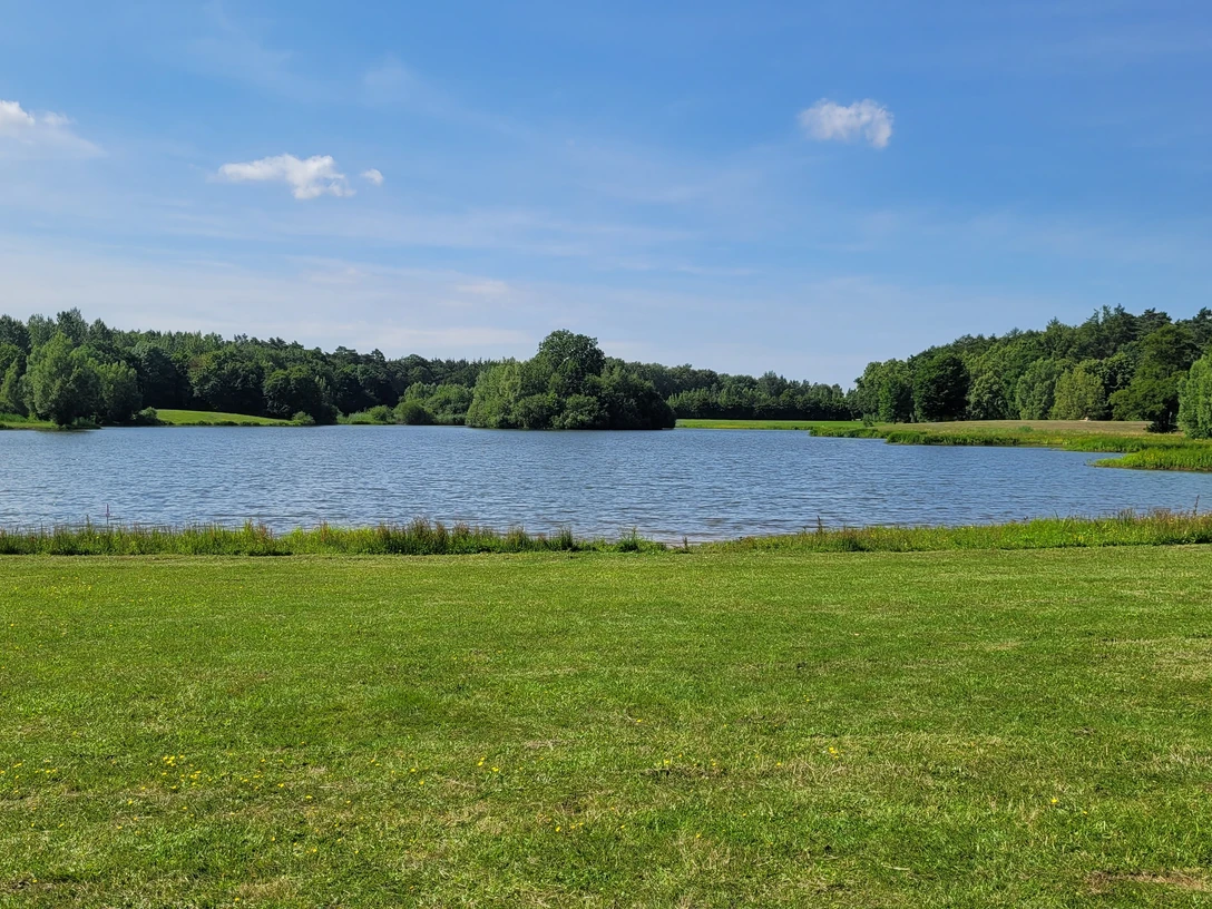 Kleihügelsee Ein kleiner See inmitten grüner Wiesen und Wälder, eingebettet in eine friedliche Naturkulisse.