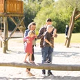 Eine Familie balanciert auf einem Baumstammspielgerät in einem sonnenverwöhnten Spielplatz.