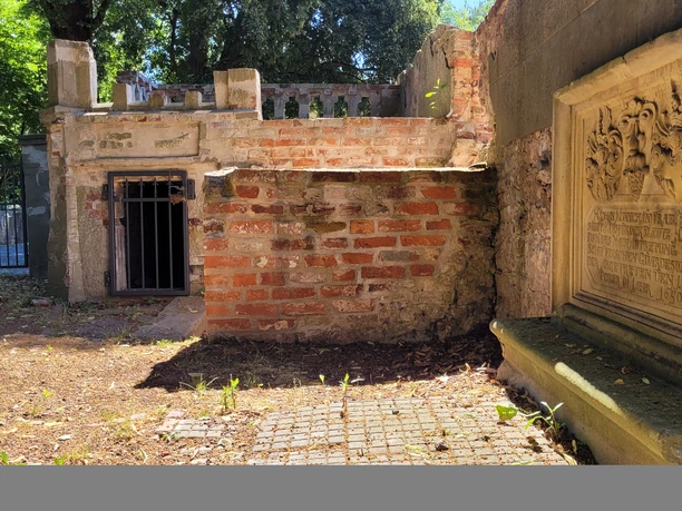 Ellerburg Alte Ziegelstruktur mit einer vergitterten Tür und Gedenktafel, umgeben von Bäumen und Laub.