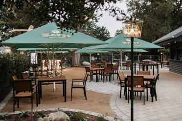 Rustige biertuin met houten stoelen onder groene parasols in een verharde buitenruimte.