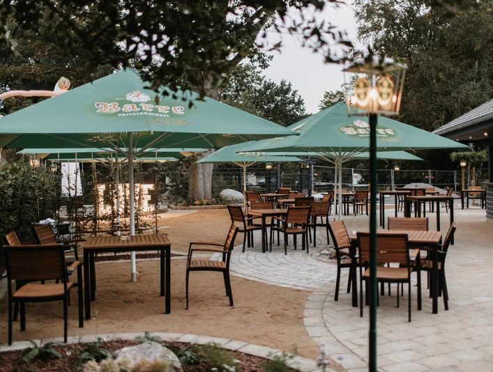 Biergarten Schneiders am Museumshof Rahden Ruhiger Biergarten mit Holzstühlen unter grünen Sonnenschirmen in einem gepflasterten Außenbereich.