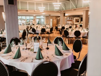 Ein großzügiger Bankettsaal mit elegant eingedeckten runden Tischen und festlicher Beleuchtung.