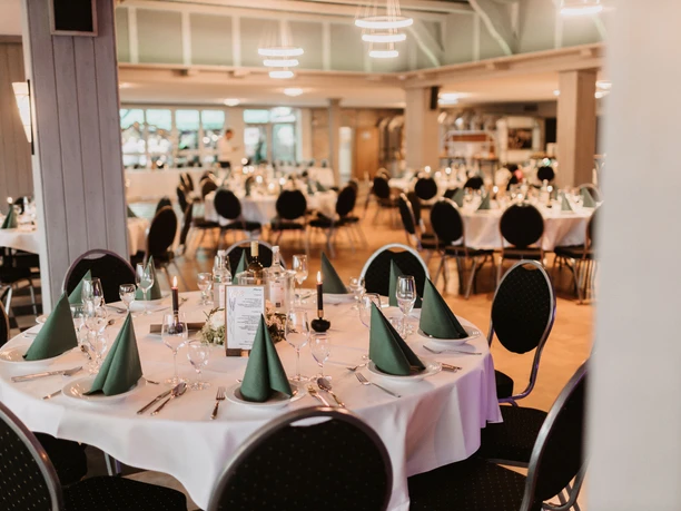 A spacious banquet hall with elegantly set round tables and festive lighting.