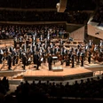 Das Bild zeigt die Berliner Philharmoniker in einem modernen Saal, umgeben von einem aufmerksamen Publikum.