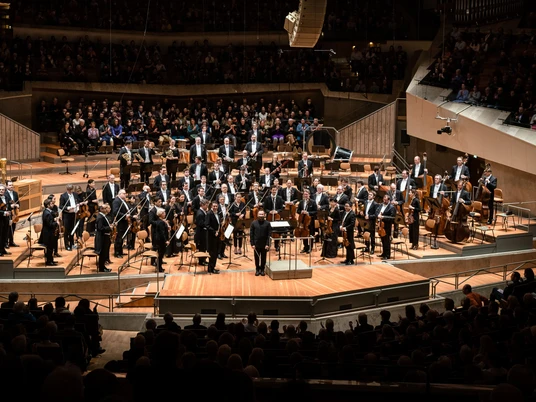 Berliner Philharmoniker Das Bild zeigt die Berliner Philharmoniker in einem modernen Saal, umgeben von einem aufmerksamen Publikum.