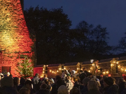 Beleuchteter Innenhof der Burg Frankenberg bei Dunkelheit mit geschmücktem Tannenbaum und vielen Besuchenden.