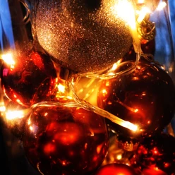 Leuchtende Weihnachtskugeln, gold und rot, in Nahaufnahme mit warmen Lichterketten umgeben.