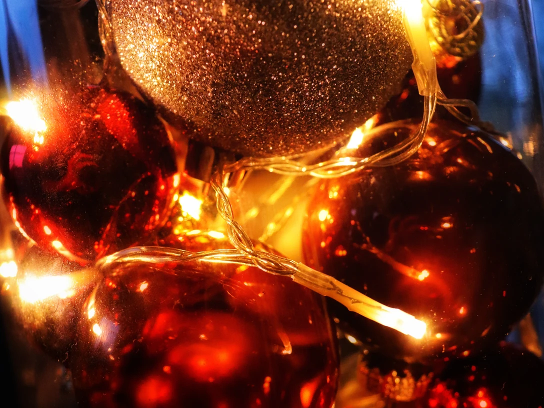 weihnachten.jpg Leuchtende Weihnachtskugeln, gold und rot, in Nahaufnahme mit warmen Lichterketten umgeben.