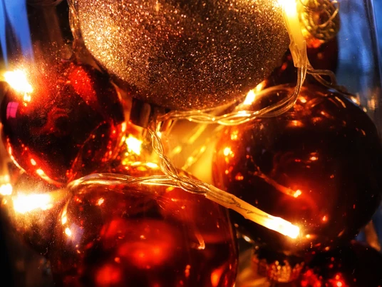 weihnachten.jpg Leuchtende Weihnachtskugeln, gold und rot, in Nahaufnahme mit warmen Lichterketten umgeben.