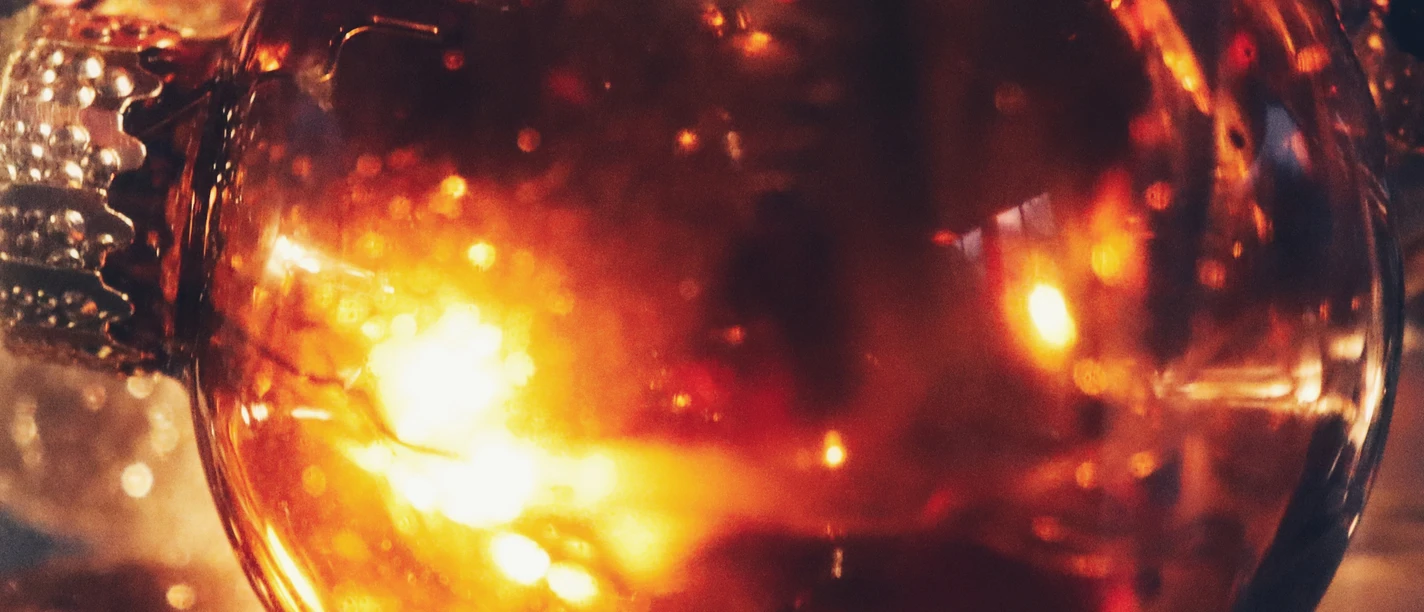 Glänzende Weihnachtskugel in warmen Goldtönen reflektiert stimmungsvoll das Kerzenlicht.