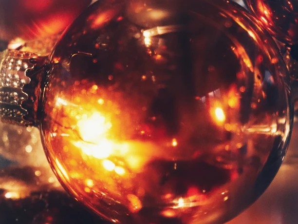 advent.jpg Glänzende Weihnachtskugel in warmen Goldtönen reflektiert stimmungsvoll das Kerzenlicht.