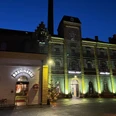 BRAUWELT KÖLN Abendlicher Blick auf eine beleuchtete, historische Backsteinbrauerei mit Eingang zur Brennerei.Evening view of an illuminated, historic brick brewery with entrance to the distillery.