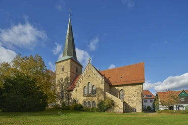 Sankt Laurentius in Bissendorf Historic church with a pointed tower and red roof, surrounded by trees under a blue sky.
