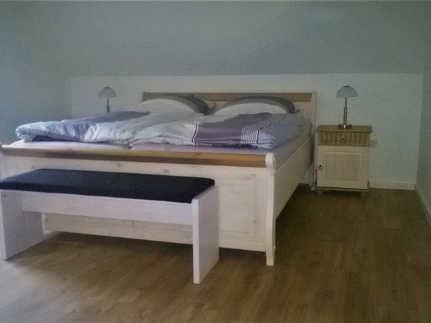 Ferienwohnung Niebaum Schlafzimmer Gemütliches Schlafzimmer mit Doppelbett aus Holz, zwei Nachttischen, Lampen und hellem Holzboden.