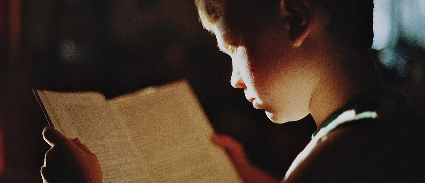 Junge liest konzentriert ein Buch im warmen Licht.