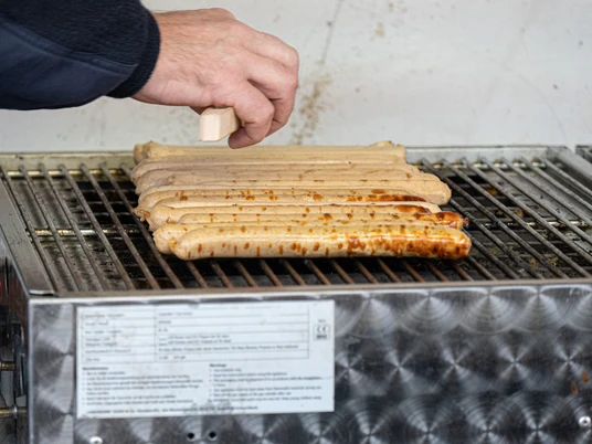 2022- Wiefelsteder Weihnachtszauber (5).jpg Mehrere Bratwürste liegen auf einem Grill. Eine Hand dreht eine Wurst mit einer Zange.
