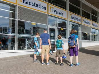 Radstation Köln Familie vor der Radstation in Köln mit Fahrradhelmen blickt auf Fahrräder hinter großen Fenstern.Family in front of the bike station in Cologne with bicycle helmets looking at bicycles behind large windows.