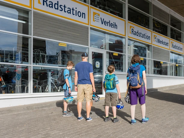 Radstation Köln Familie vor der Radstation in Köln mit Fahrradhelmen blickt auf Fahrräder hinter großen Fenstern.