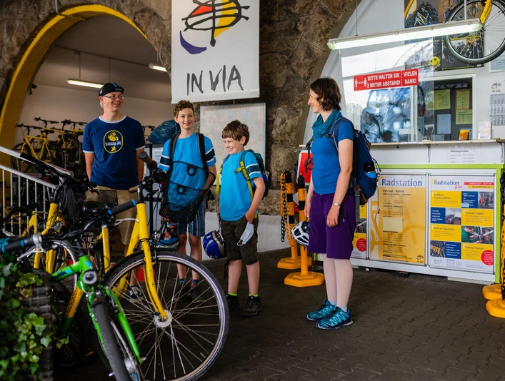 Cologne bike station Vier Personen in Freizeitkleidung, mit Fahrrädern vor einem Informationsschalter.Four people in casual clothes, with bicycles in front of an information desk.
