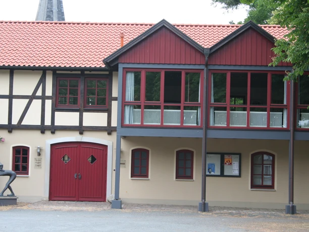 Bürgerhaus Uchte Fachwerkgebäude mit rotem Ziegeldach und Holzverzierungen, darüber befindet sich ein verglaster Balkon.