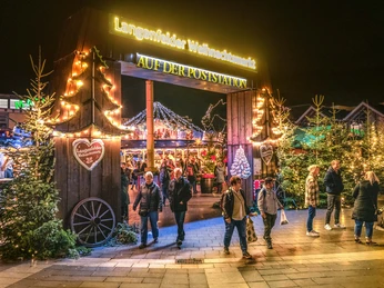 Langenfelder Weihnachtsdorf Weihnachtsmarkt mit festlich beleuchteten Ständen, geschäftigen Besuchenden und Tannenbäumen bei Nacht.