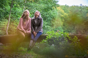 Waldspaziergang_AlexKMedia (2).jpg Zwei Frauen sitzen im Wald auf einem Baumstamm