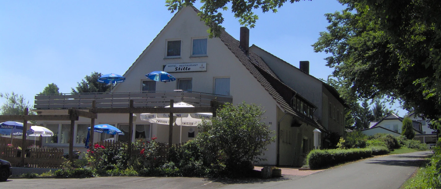 Hotel Stille Aussenansicht Zweistöckiges Hotel mit Holzbalkon und Terrasse, umgeben von üppigem Grün und Sonnenschirmen.