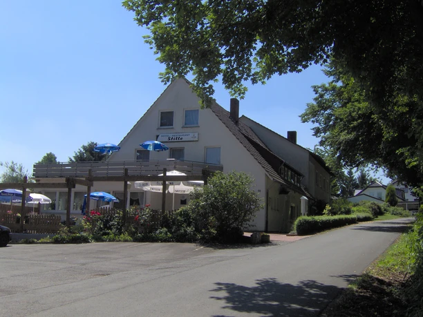 Hotel Stille Aussenansicht Zweistöckiges Hotel mit Holzbalkon und Terrasse, umgeben von üppigem Grün und Sonnenschirmen.