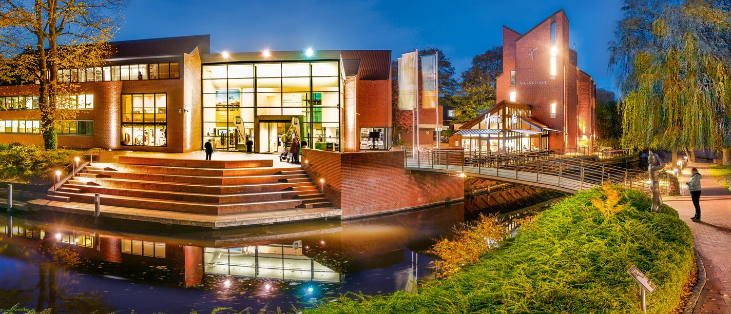 Kunsthalle-Emden_Foto-Bühler -141.jpg Exterior view of the Kunsthalle in the evening. The entrance is on a wide staircase, with trees and canals in the background."