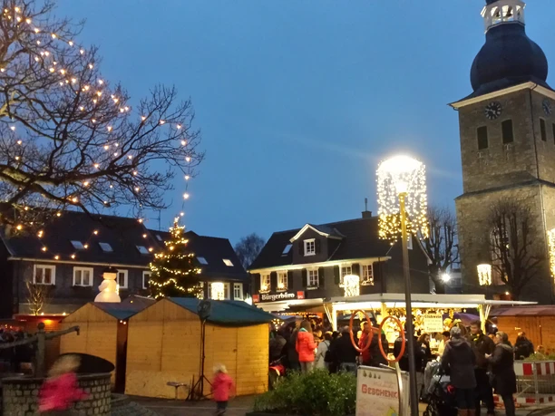 Radevormwalder Weihnachtsmarkt Abendlicher Weihnachtsmarkt mit Buden, geschmücktem Baum und im Hintergrund eine Kirche mit Turm.