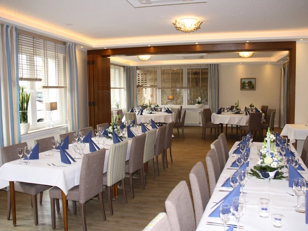 Festlich gedeckter, moderner Speisesaal mit weißen Tischdecken, blauen Servietten und Blumenarrangements.