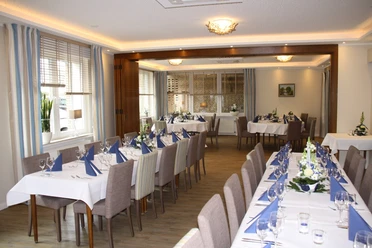 Gaststaette.jpg Festlich gedeckter, moderner Speisesaal mit weißen Tischdecken, blauen Servietten und Blumenarrangements.
