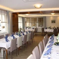 Gaststaette.jpg Festlich gedeckter, moderner Speisesaal mit weißen Tischdecken, blauen Servietten und Blumenarrangements.
