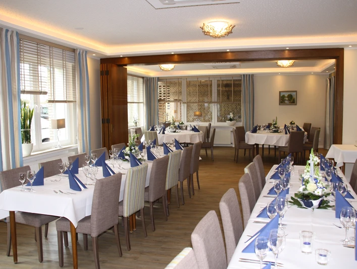 Gaststaette.jpg Festlich gedeckter, moderner Speisesaal mit weißen Tischdecken, blauen Servietten und Blumenarrangements.