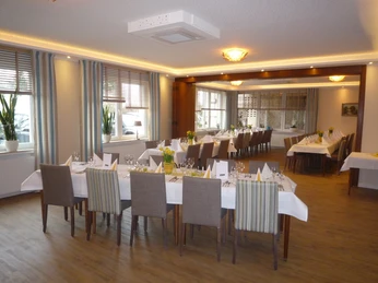 Helles Restaurant mit gedeckten Tischen, Holzfußboden und großen Fenstern mit gestreiften Vorhängen.