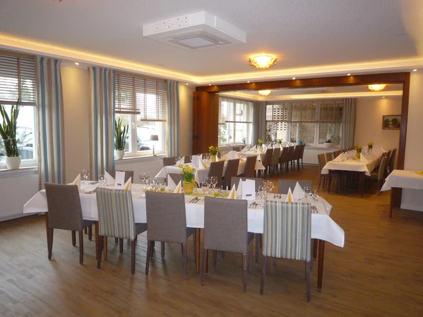 Helles Restaurant mit gedeckten Tischen, Holzfußboden und großen Fenstern mit gestreiften Vorhängen.