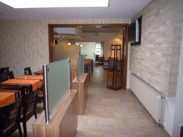 Moderner Speiseraum mit Holzmöbeln, orange Tischdecken und heller, gemusterter Wandgestaltung.