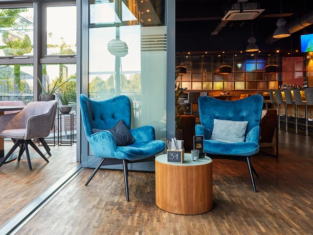 Heiners_Cloud7, Gelsenkirchen <p>Zwei blaue Sessel und ein Tisch stehen vor großen Fenstern in einem modernen Café oder Restaurant.</p>