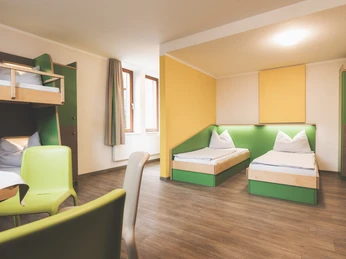 Familienzeit2 CR Jugendherberge Lingen.jpg Helles Familienzimmer mit Etagenbett und Einzelbetten, grünen Akzenten und warmem Holzfußboden