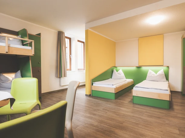 Familienzeit2 CR Jugendherberge Lingen.jpg Helles Familienzimmer mit Etagenbett und Einzelbetten, grünen Akzenten und warmem Holzfußboden